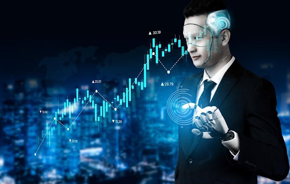 A human-like robot wearing a business suit and a prosthetic hand is shown from the chest up, interacting with a glowing circular interface on its fingertips. Its face and head have translucent elements revealing circuit patterns and gears. In the background, a blue-toned stock market bar graph with an upward trend and various numerical indicators (e.g., 25.01, 30.19) overlays a blurred cityscape.