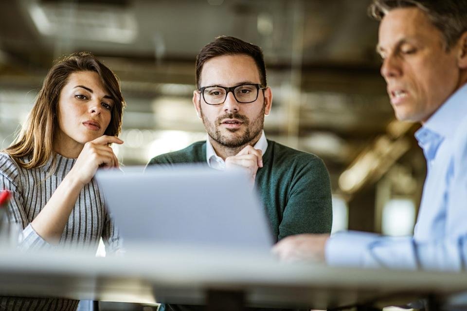 Three investors seated around a laptop discuss some data.